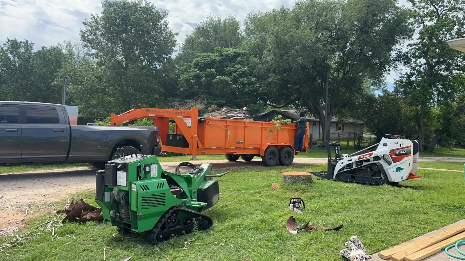 Stump grinding work area with grinder, loader, trailer, and crew