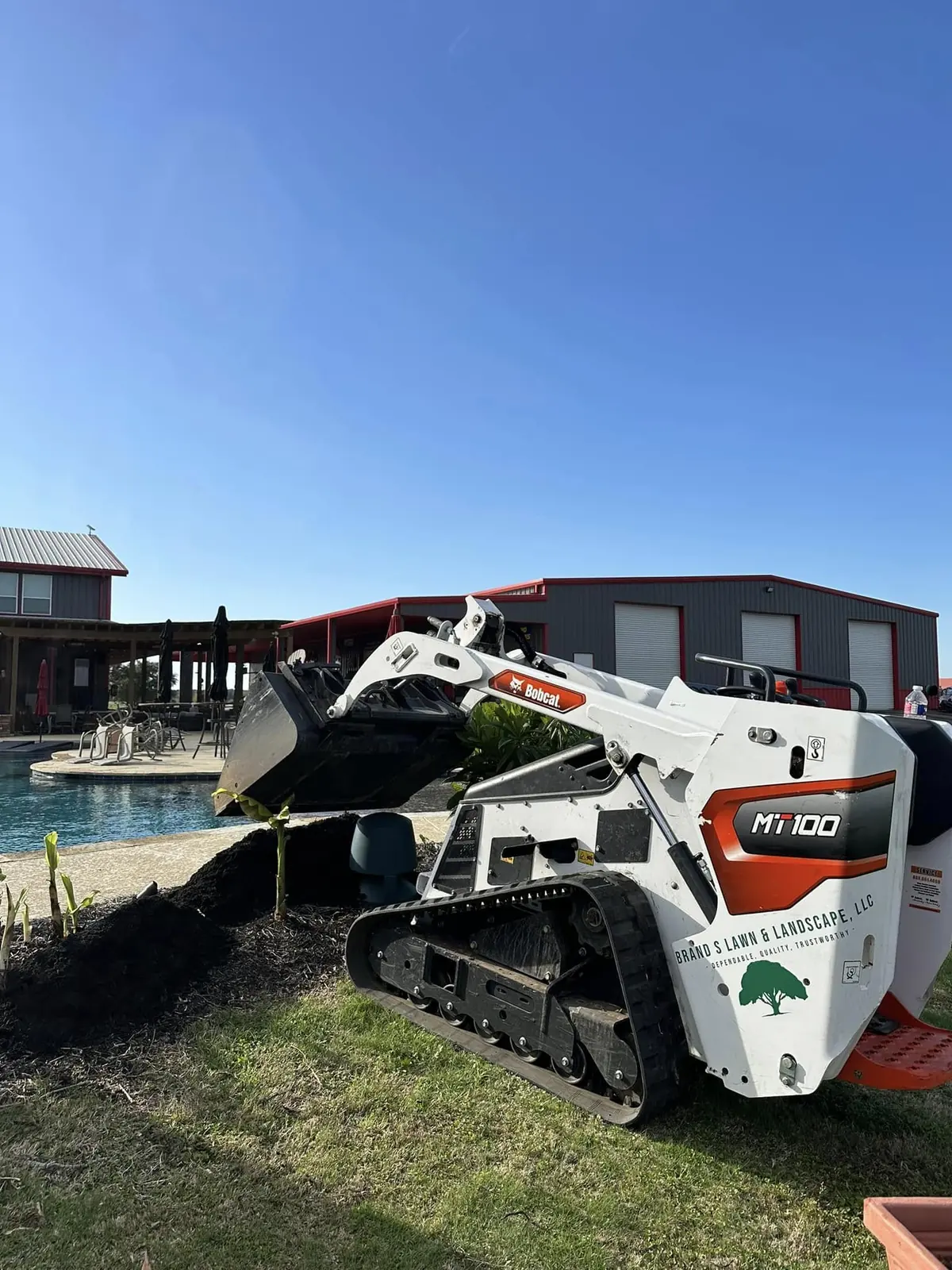 Skid-steer placing material in a poolside planting bed