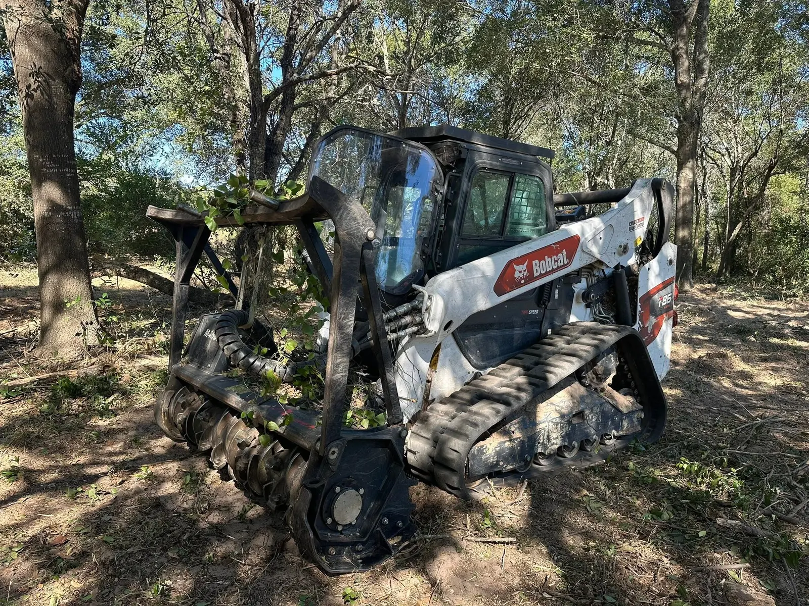 Skid steer clearing branches at a wooded project site